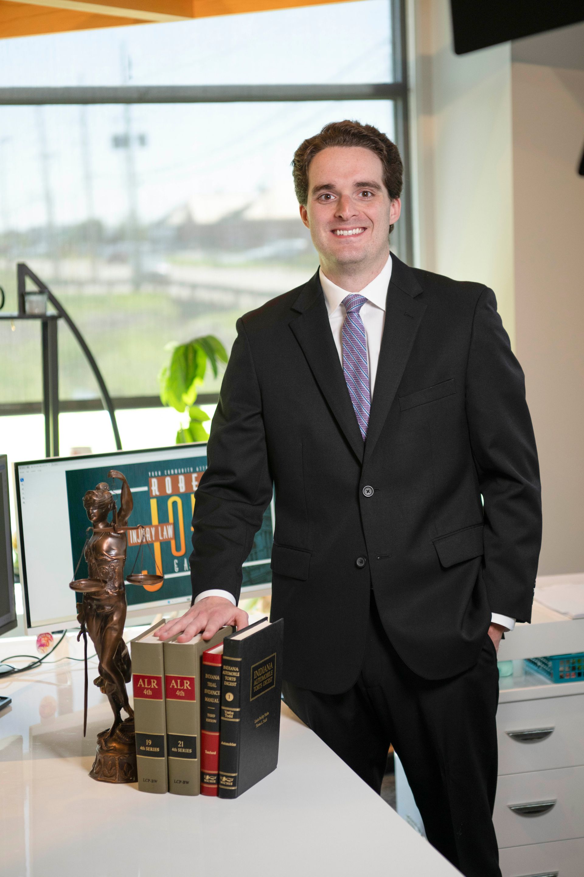 William “Will” Marshall standing in office with law books, Lady Justice, and firm branding.