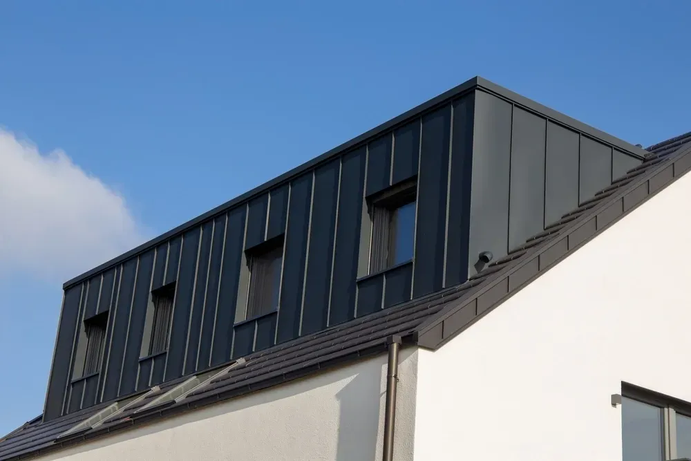 Dark gray metal roof with dormer windows against a blue sky. — Your Craftsmen in Cardiff, NSW