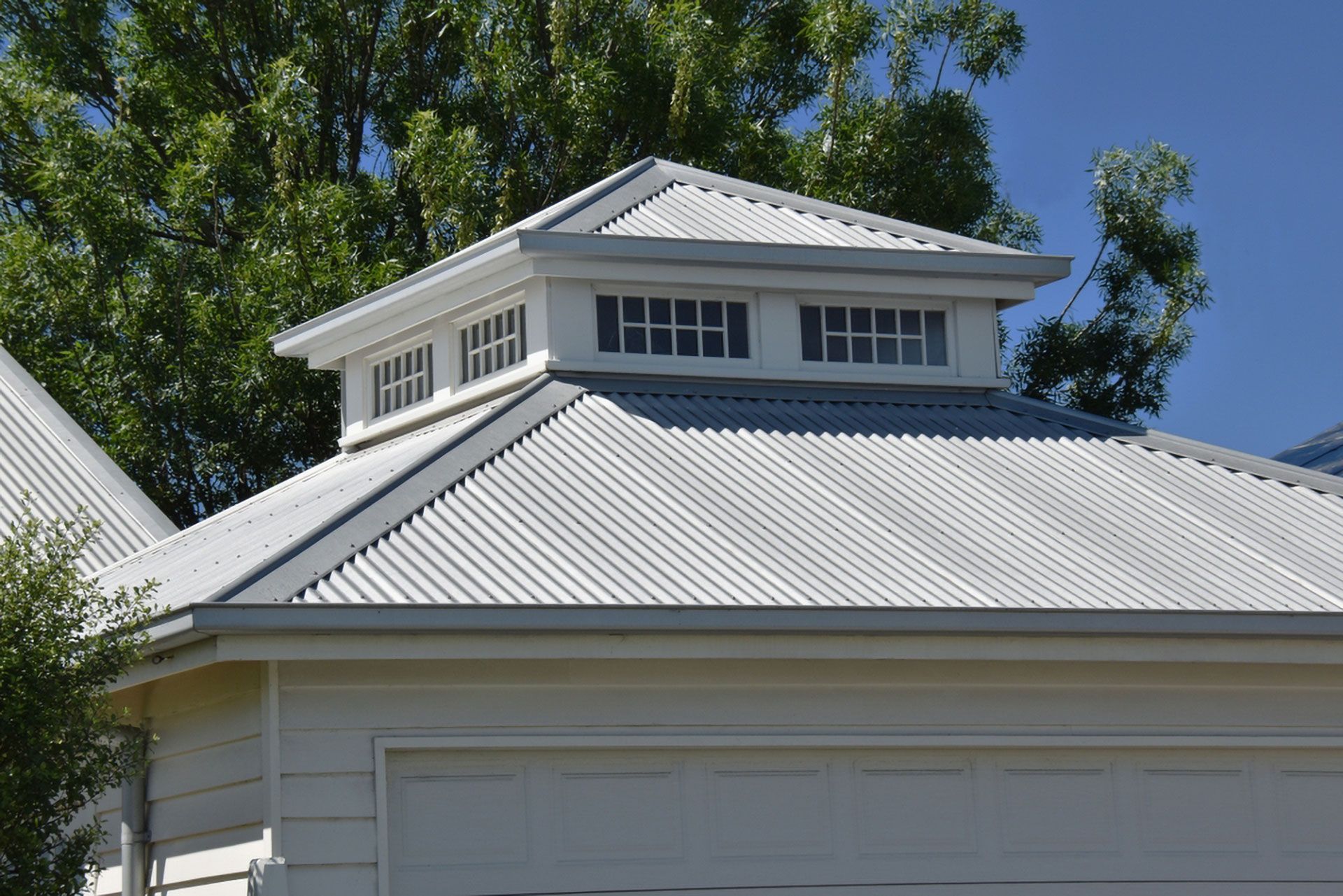 White Building With Corrugated Metal Roof and a Cupola With Small Windows Blue Sky — Your Craftsmen in Eleebana, NSW