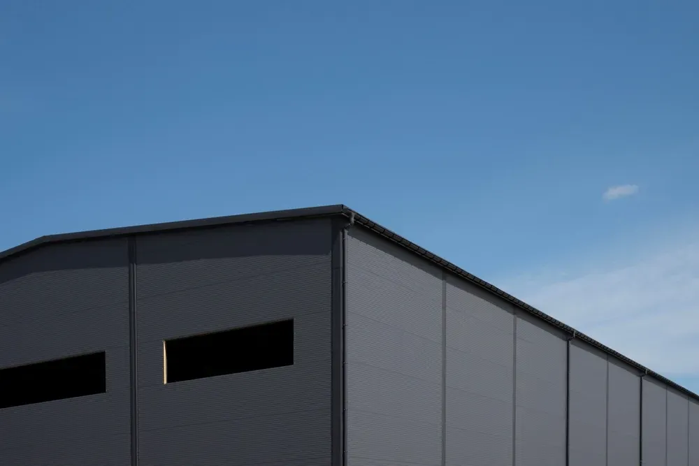 Dark gray industrial building against a clear blue sky, with rectangular windows. — Your Craftsmen in Newcastle, NSW