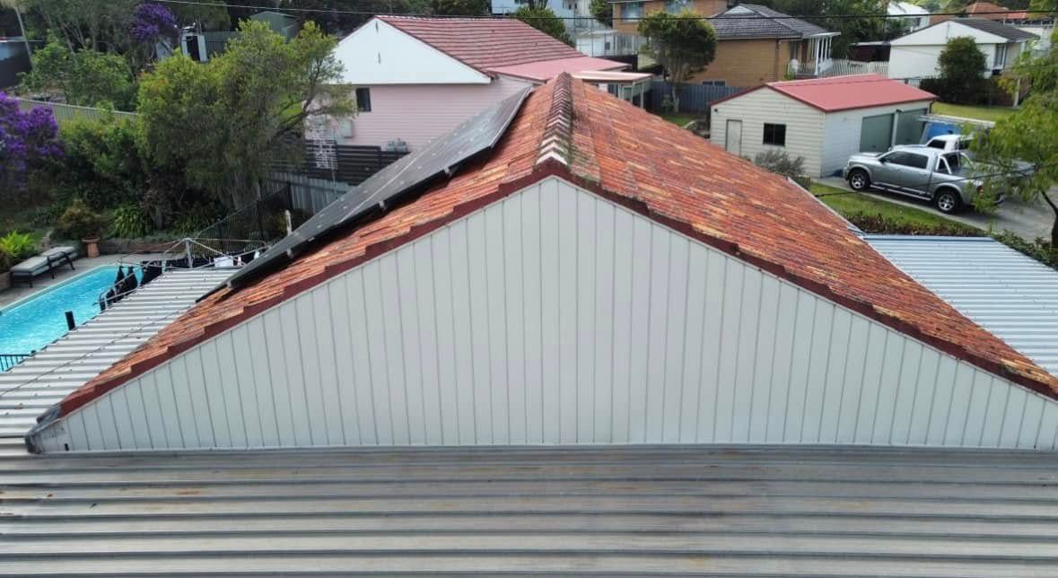 A Triangular Roof With Red Tiles and White Siding. Solar Panels Sit on the Roof's Peak — Your Craftsmen in Eleebana, NSW