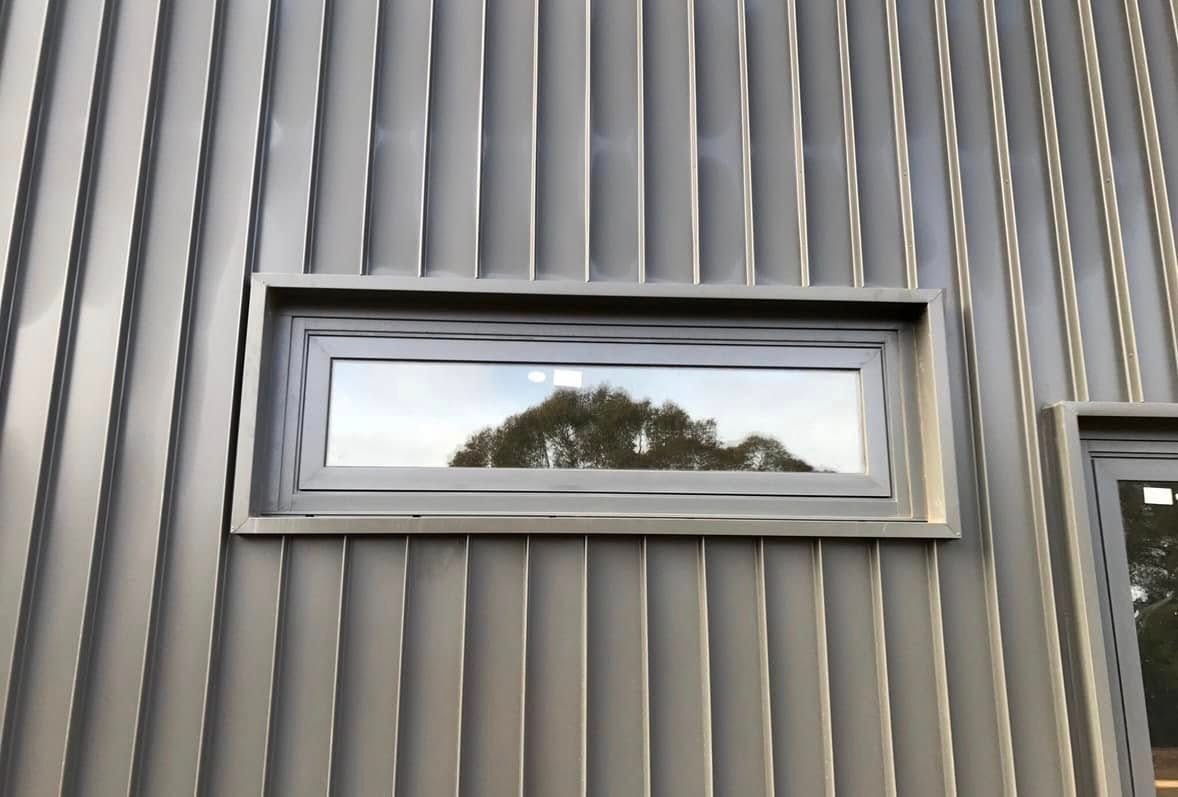 Rectangular window set in grey corrugated metal siding, reflecting a tree. — Your Craftsmen in Toronto, NSW