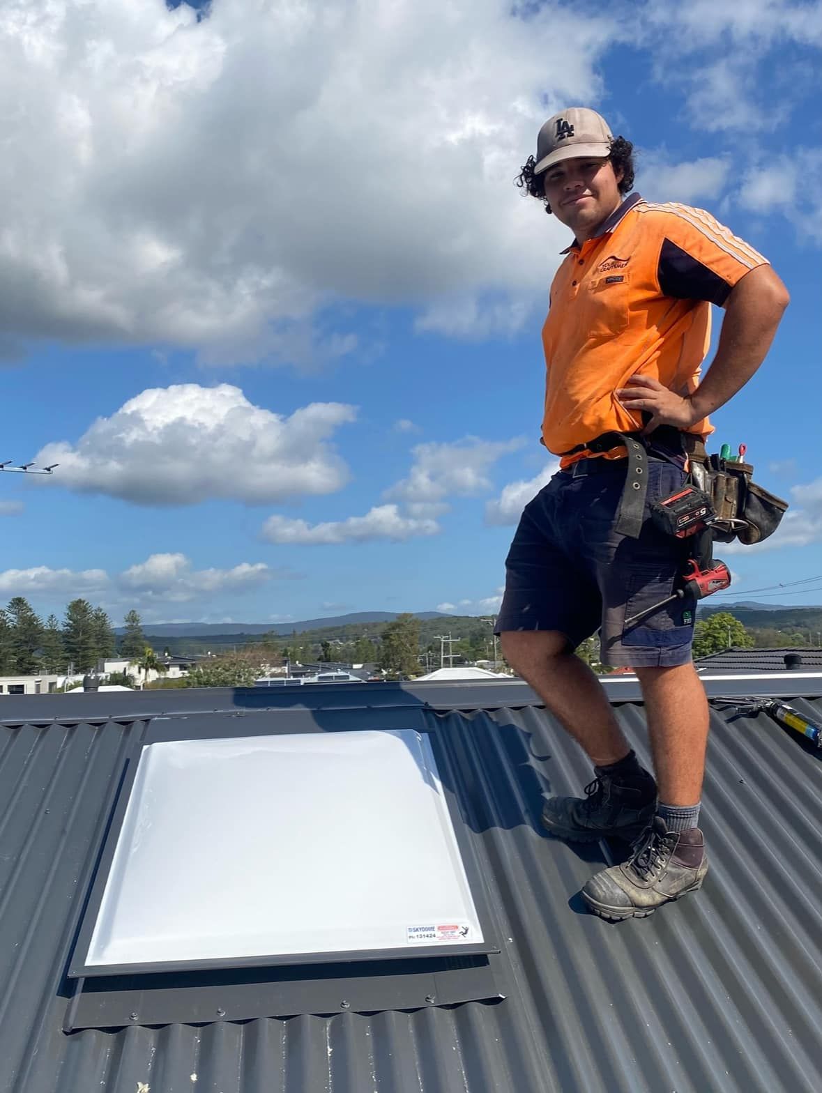 Roofer Stands on a Corrugated Metal Roof Next to a Skylight on a Sunny Day — Your Craftsmen in Cardiff, NSW
