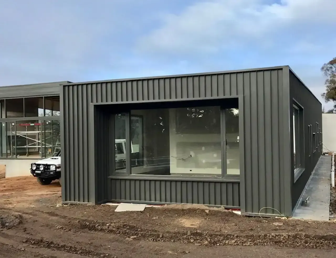 Gray Corrugated Metal Building With Large Windows, Under Construction, on a Cloudy Day — Your Craftsmen in Maitland, NSW