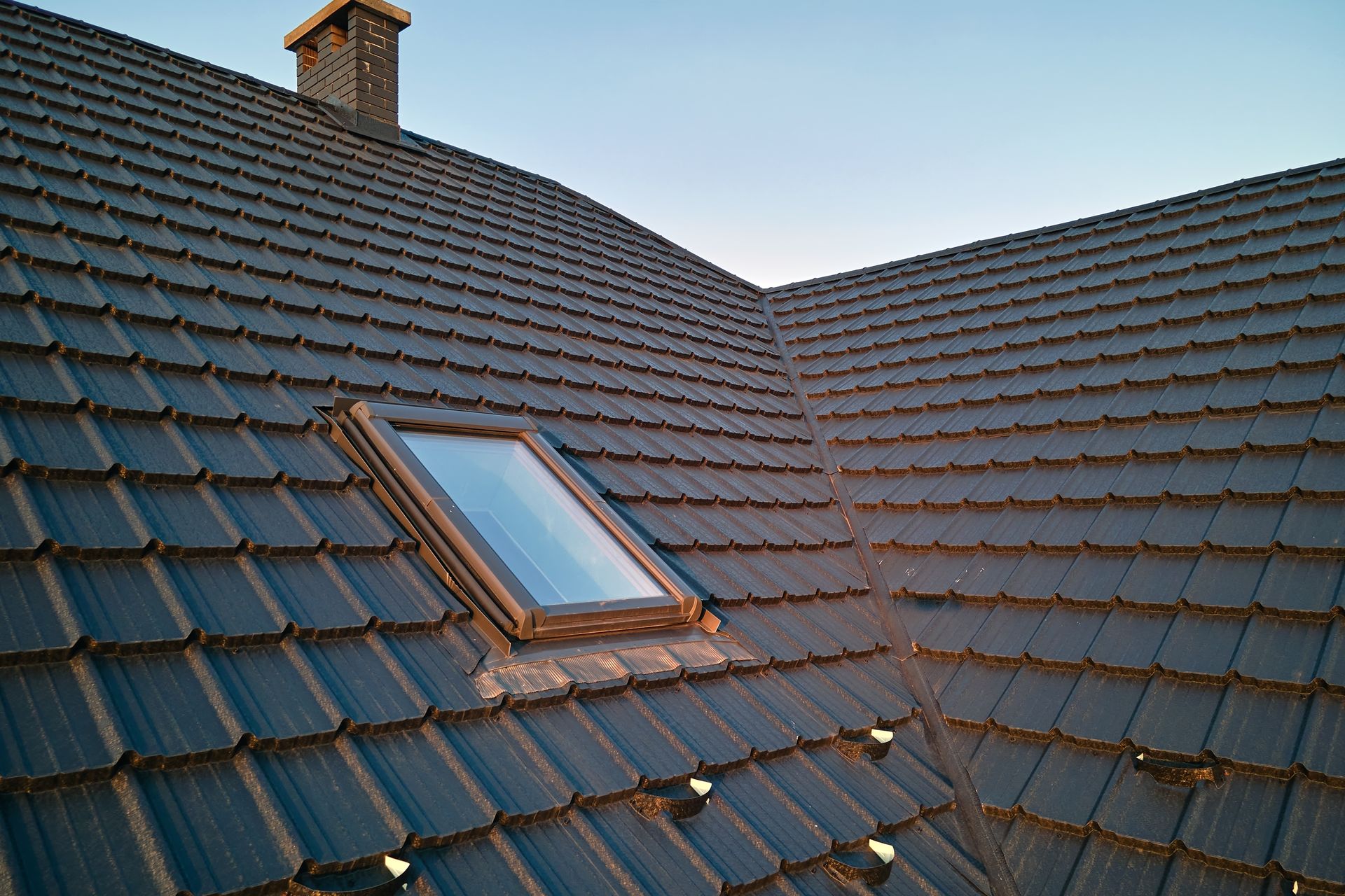 Dark Gray Tiled Roof With a Skylight and Brick Chimney Under a Blue Sky — Your Craftsmen in Wangi Wangi, NSW