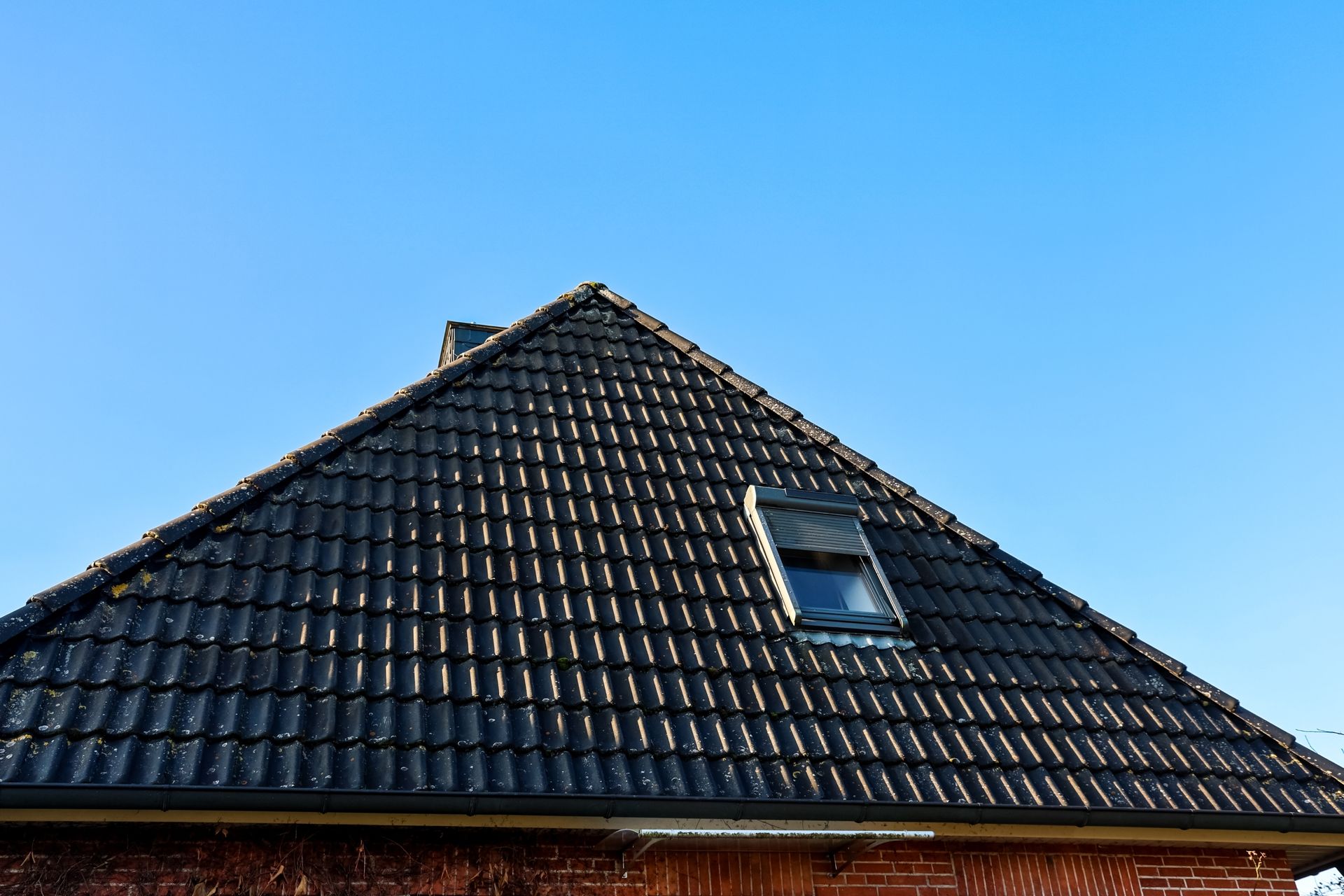 Dark Tiled Roof With Skylight Against a Clear Blue Sky — Your Craftsmen in Merewether, NSW