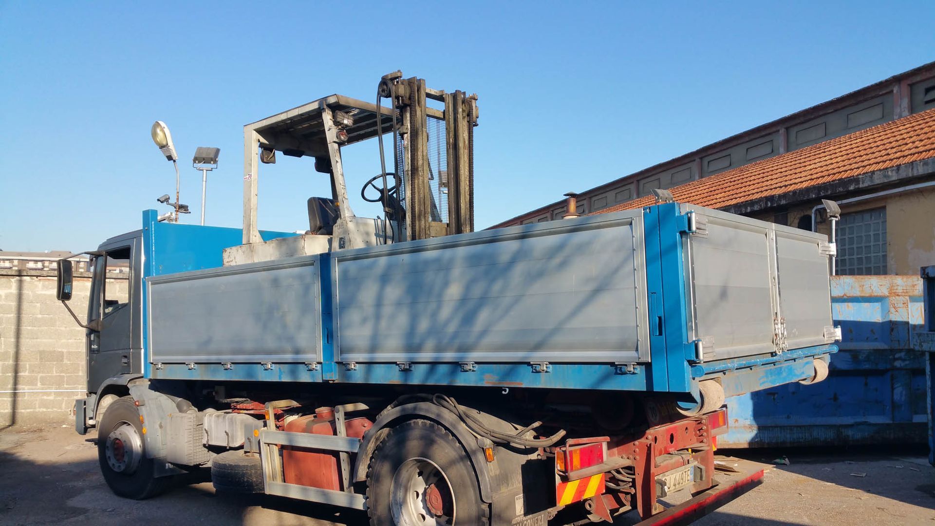 Un autocarro con cassone ribaltabile con un carrello elevatore nella parte posteriore è parcheggiato in un parcheggio.