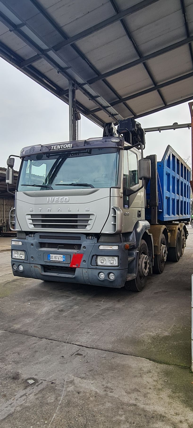 Un autocarro con cassone ribaltabile è parcheggiato sotto una tettoia in un parcheggio.