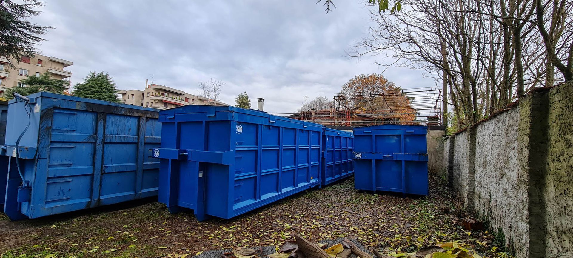 Una fila di cassonetti blu sono seduti uno accanto all'altro in un cortile.