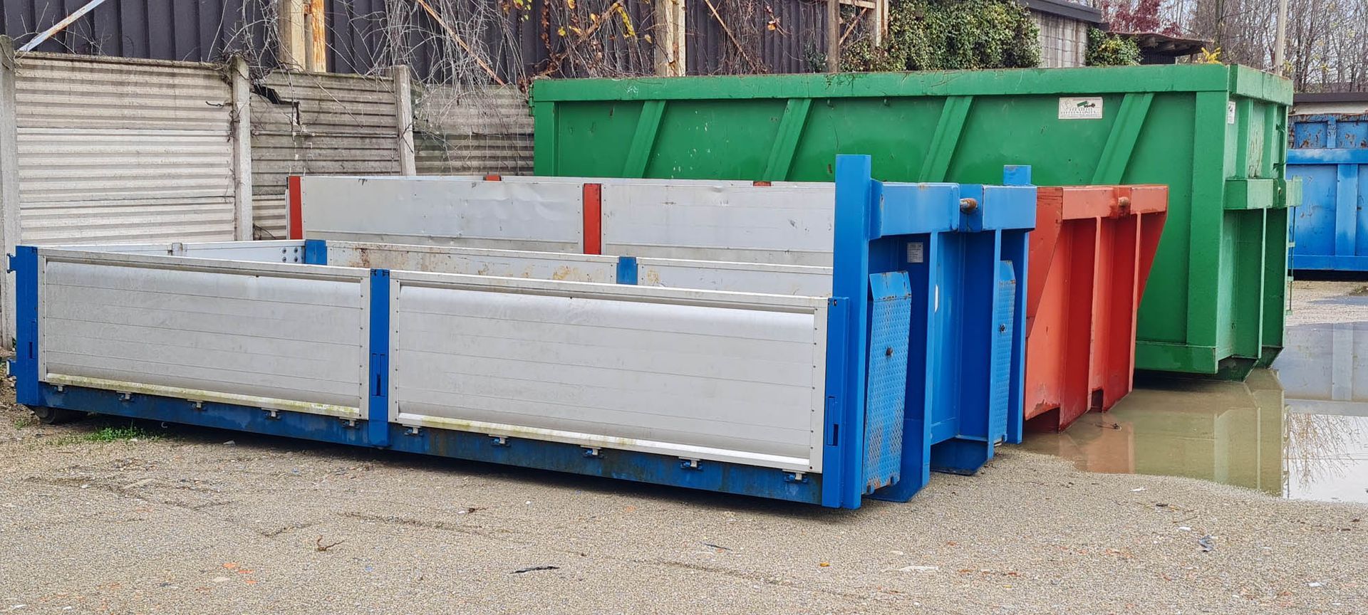 Una fila di cassonetti sono allineati in un parcheggio.