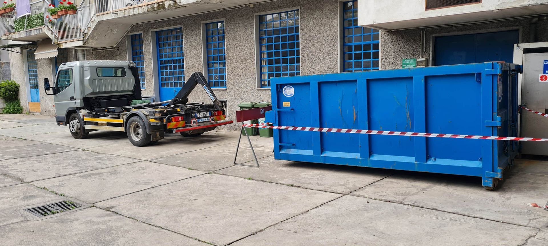 Un cassonetto blu è parcheggiato davanti a un edificio accanto a un camion.