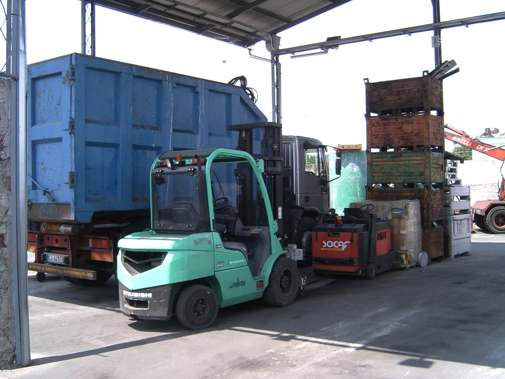 Un carrello elevatore verde è parcheggiato davanti a un autocarro con cassone ribaltabile