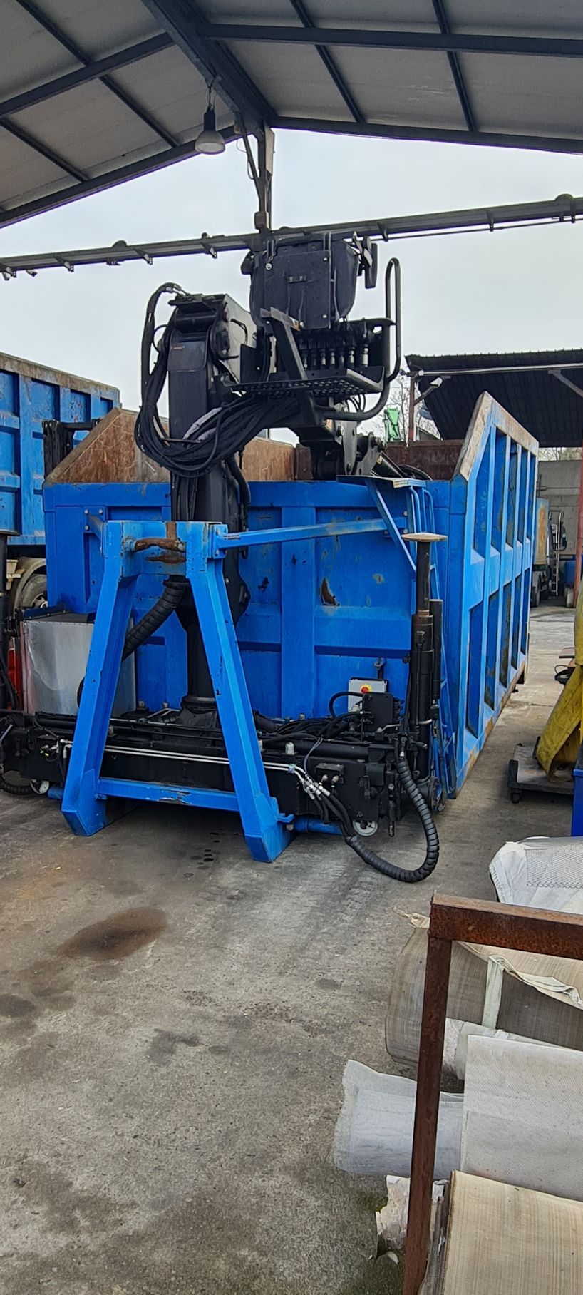 Un cassonetto blu con una gru attaccata è seduto in un parcheggio.