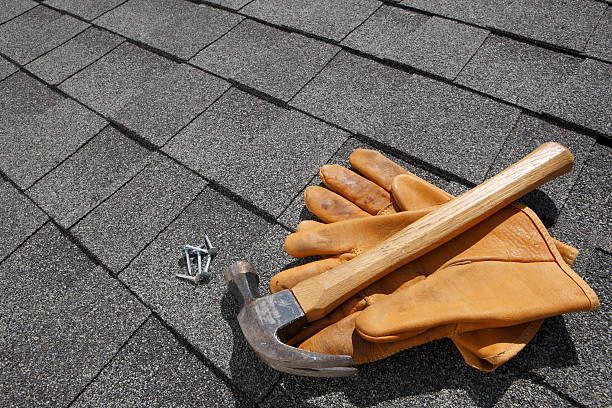 A pair of gloves , a hammer , and nails are on a roof.