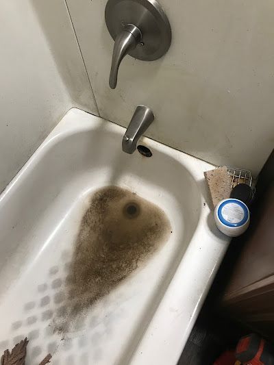 Dirty bathtub with brown stained water and a soap bottle on the edge