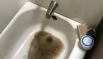 Dirty sink with brown stains, a faucet, and a small container on the right edge.