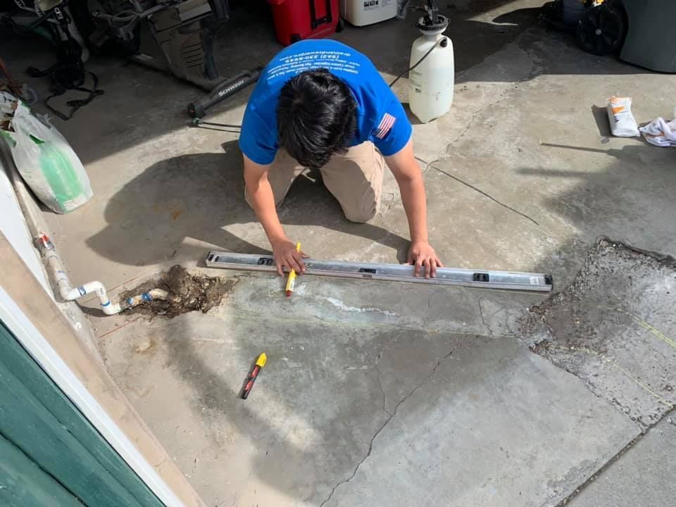 Person in a blue shirt leveling concrete with a straightedge in a garage floor.