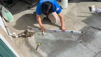 Person in blue shirt leveling wet concrete with a long straightedge outdoors.