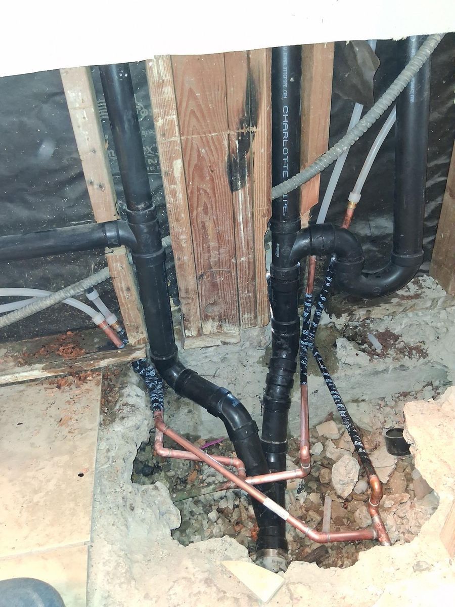 Exposed plumbing pipes and copper lines in a wall opening during construction/repair