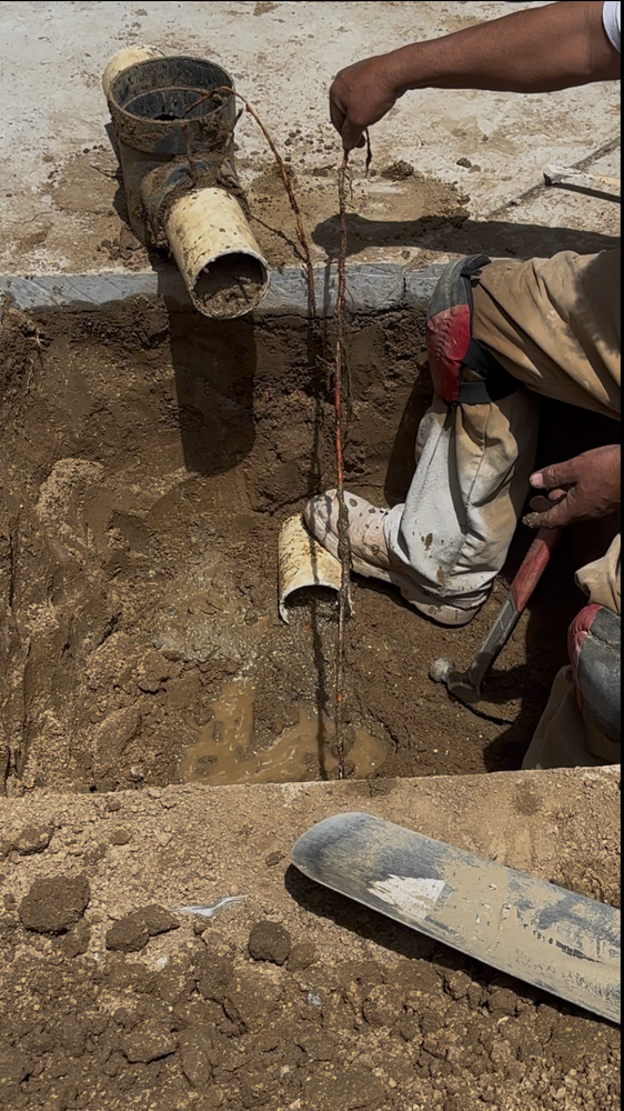 Workers repairing a broken underground pipe in muddy soil, with tools and exposed plumbing parts