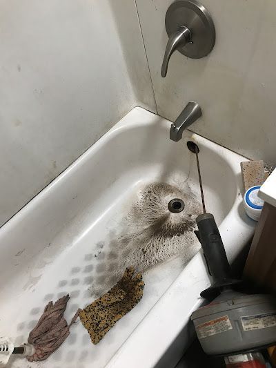 Dirty bathtub being cleaned with a scrubber and hose, with soap residue and cleaning supplies visible.