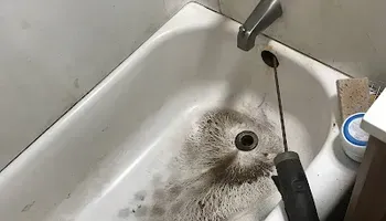 Filthy white sink with a clogged drain and dark debris near the faucet