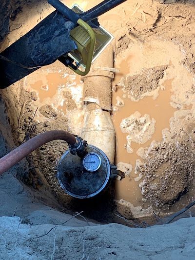 Underground utility pipe being inspected in a muddy excavation pit, with a hose attached