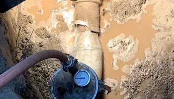 Hose connected to a water meter in a muddy underground utility pit