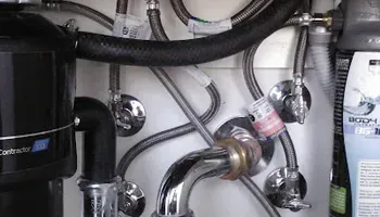 Under-sink plumbing with chrome pipes, valves, and a black water filter unit.