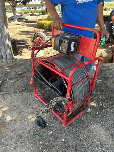 Person holding a red metal cable reel cart outdoors on a dirt ground.