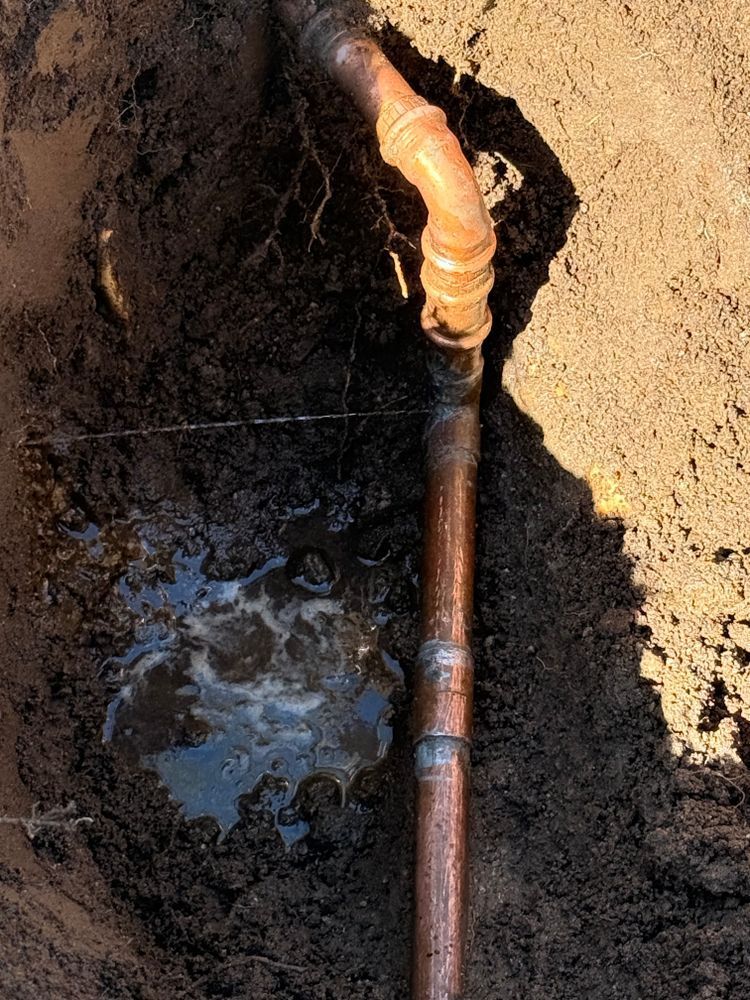 Copper pipe and elbow fitting in a narrow dirt trench with standing water.
