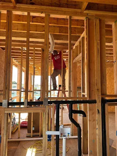 Person in a red shirt standing on a ladder inside a framed house under construction