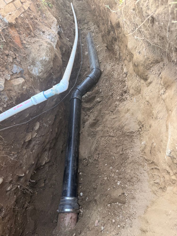 Black and white pipes joined in a dirt trench during underground utility installation