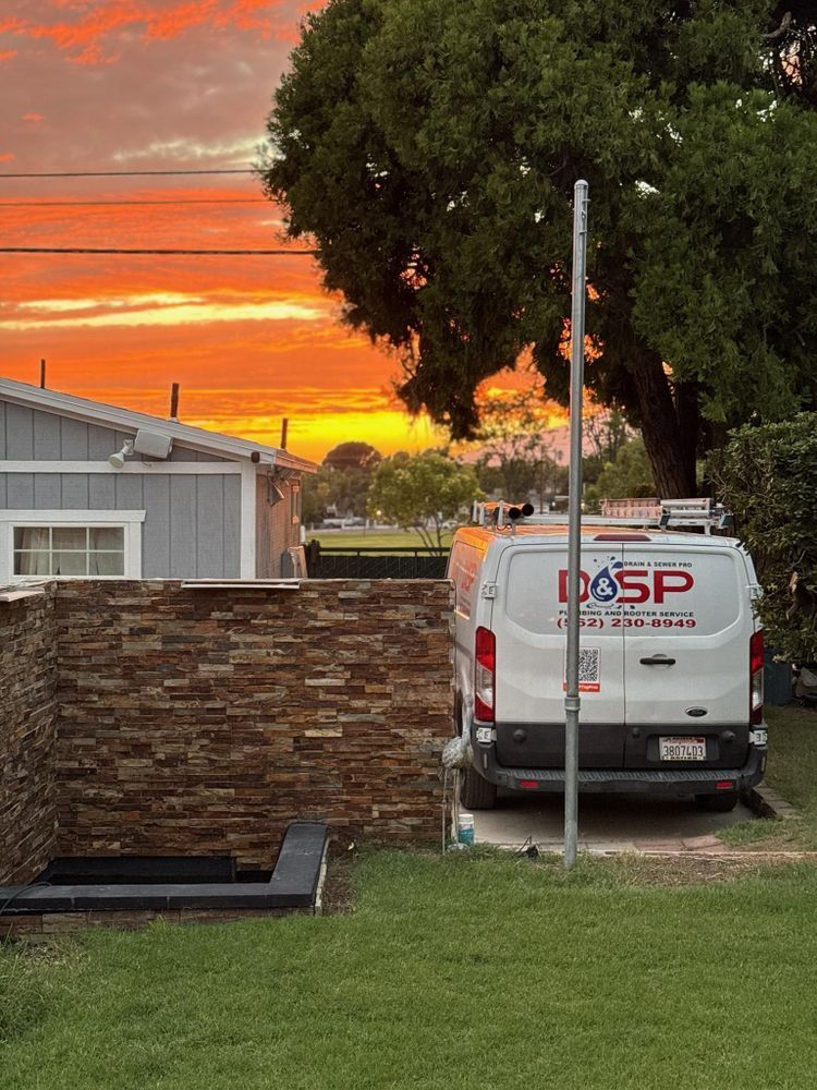 White van parked beside a stone wall at sunset, with a vivid orange sky and a large tree overhead.