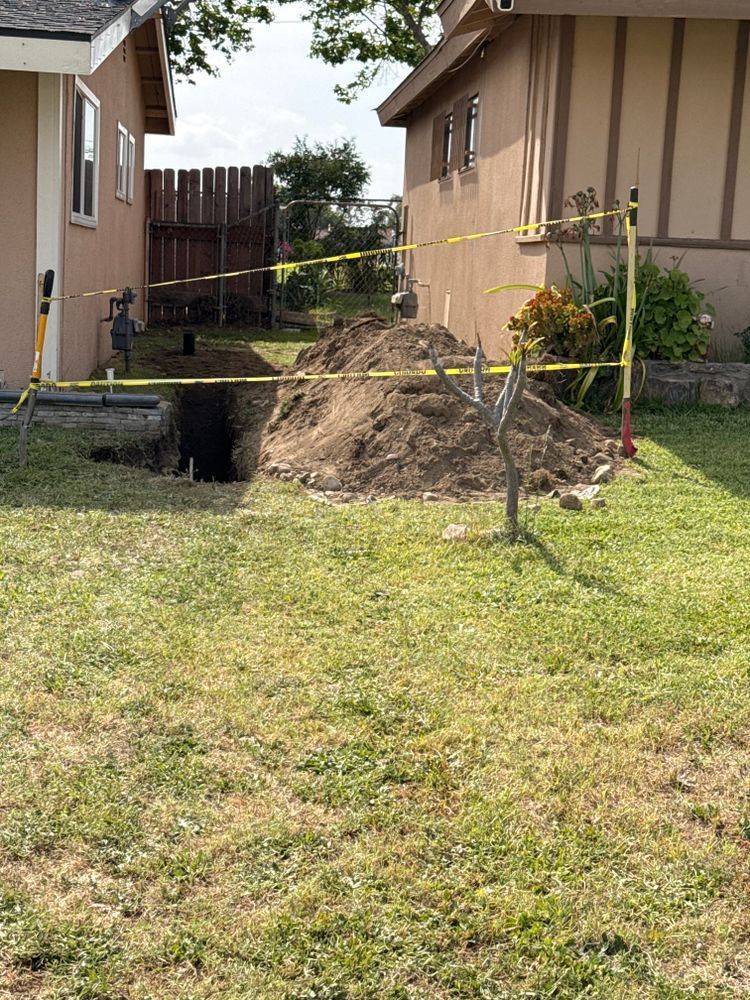 Backyard between two houses with a dirt mound and yellow caution tape around a dug-up area.