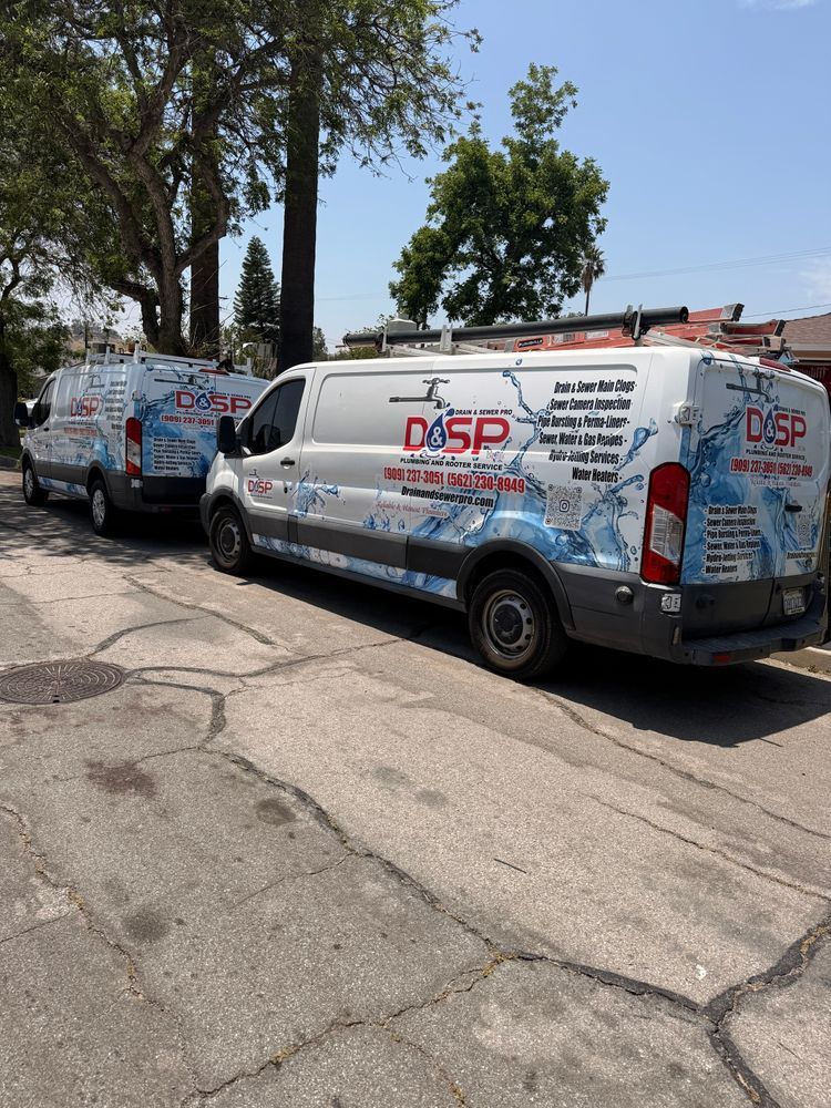 Two white and silver service vans with red and blue graphics parked along a cracked street under trees.