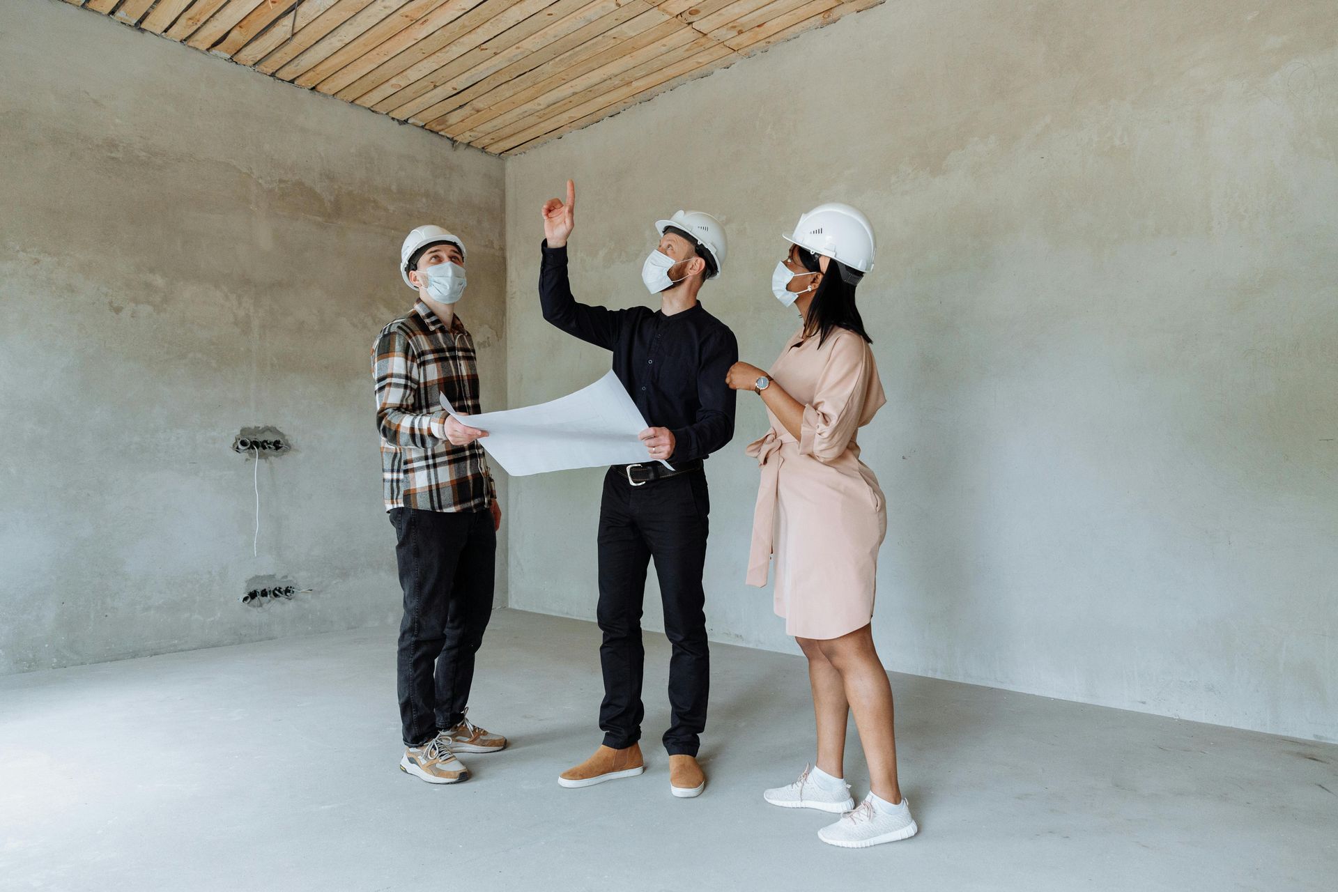 A group of people wearing masks and hard hats are standing in an empty room.