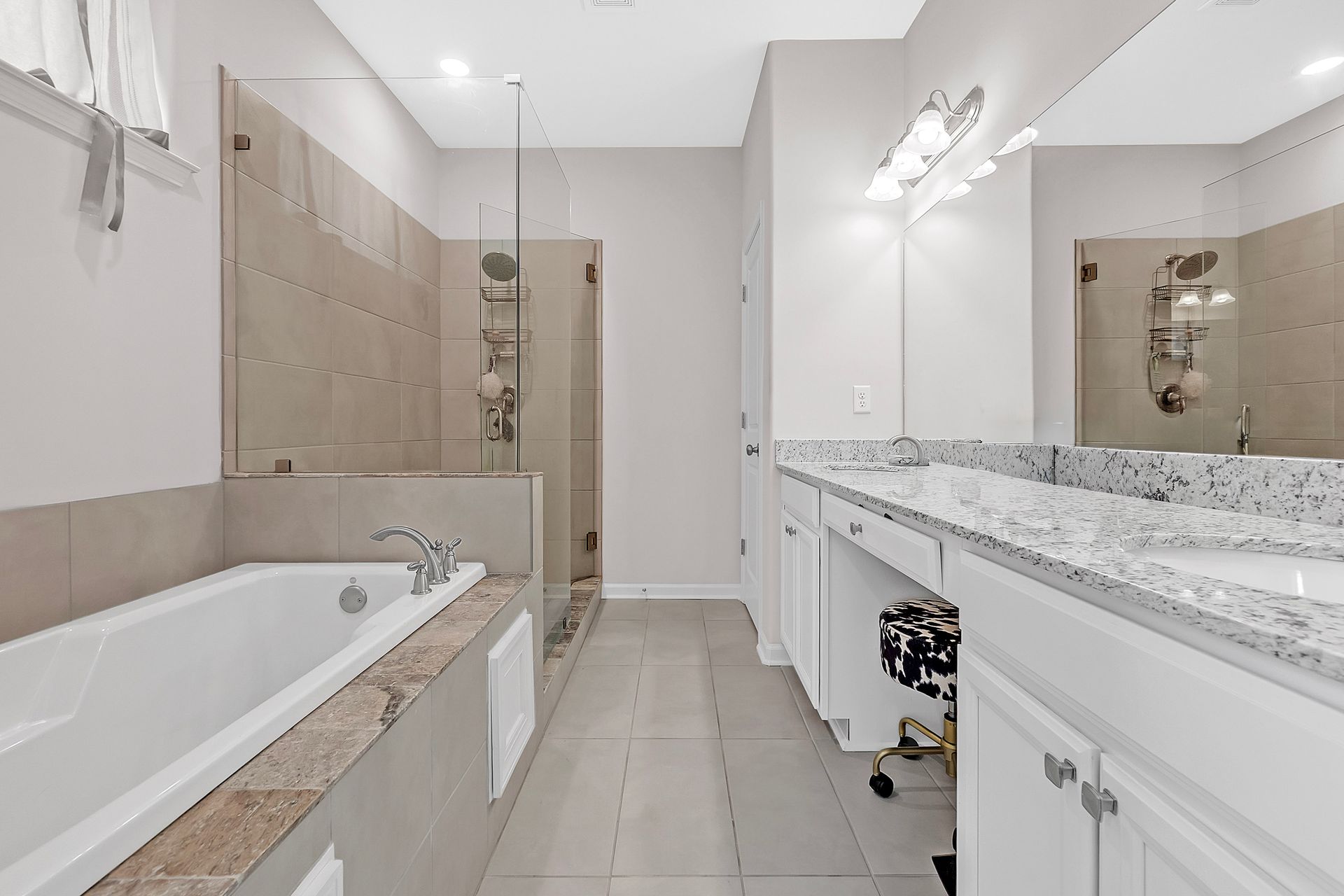 Spacious white bathroom with tub, glass shower, long vanity with granite countertop and mirror.