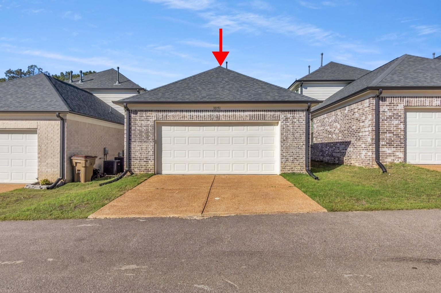 Garage with white door and dark gray roof; arrow pointing to the top. Brick exterior.
