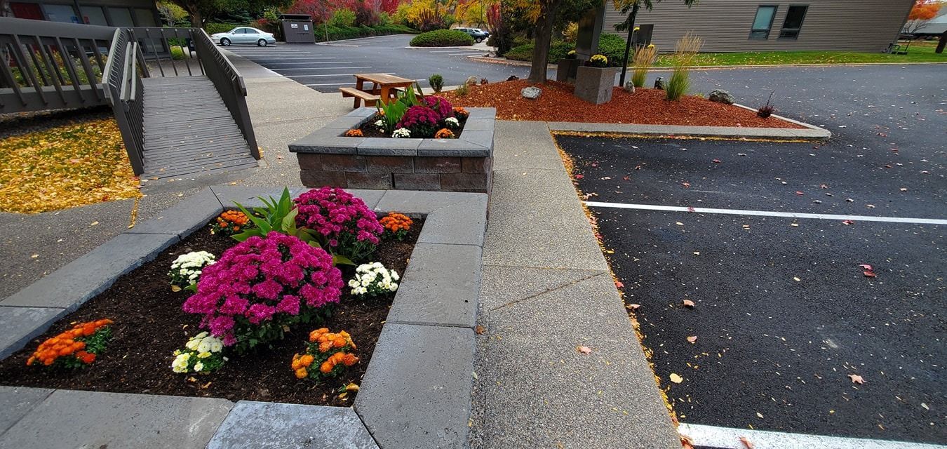 Flowerbeds border a walkway and parking area, with colorful autumn foliage.