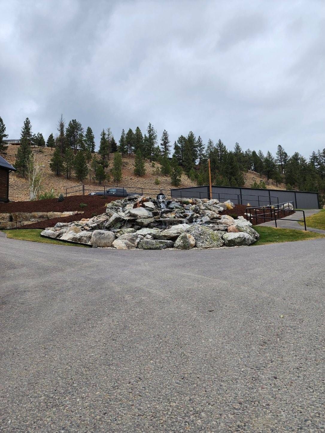 Rocky waterfall in front of a hill with trees, on a cloudy day.