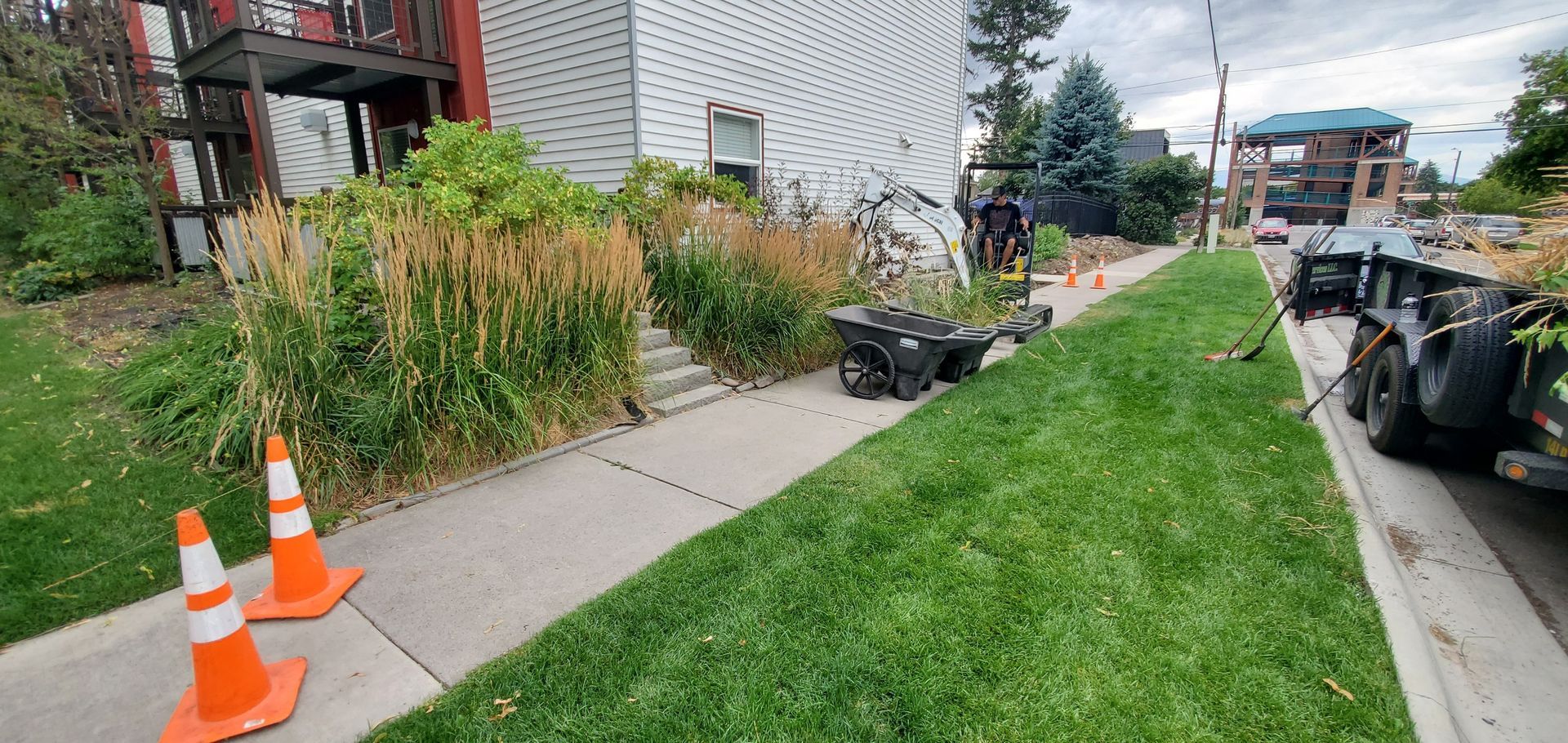 Two orange cones on a sidewalk. Lush green lawn. Landscaping workers.