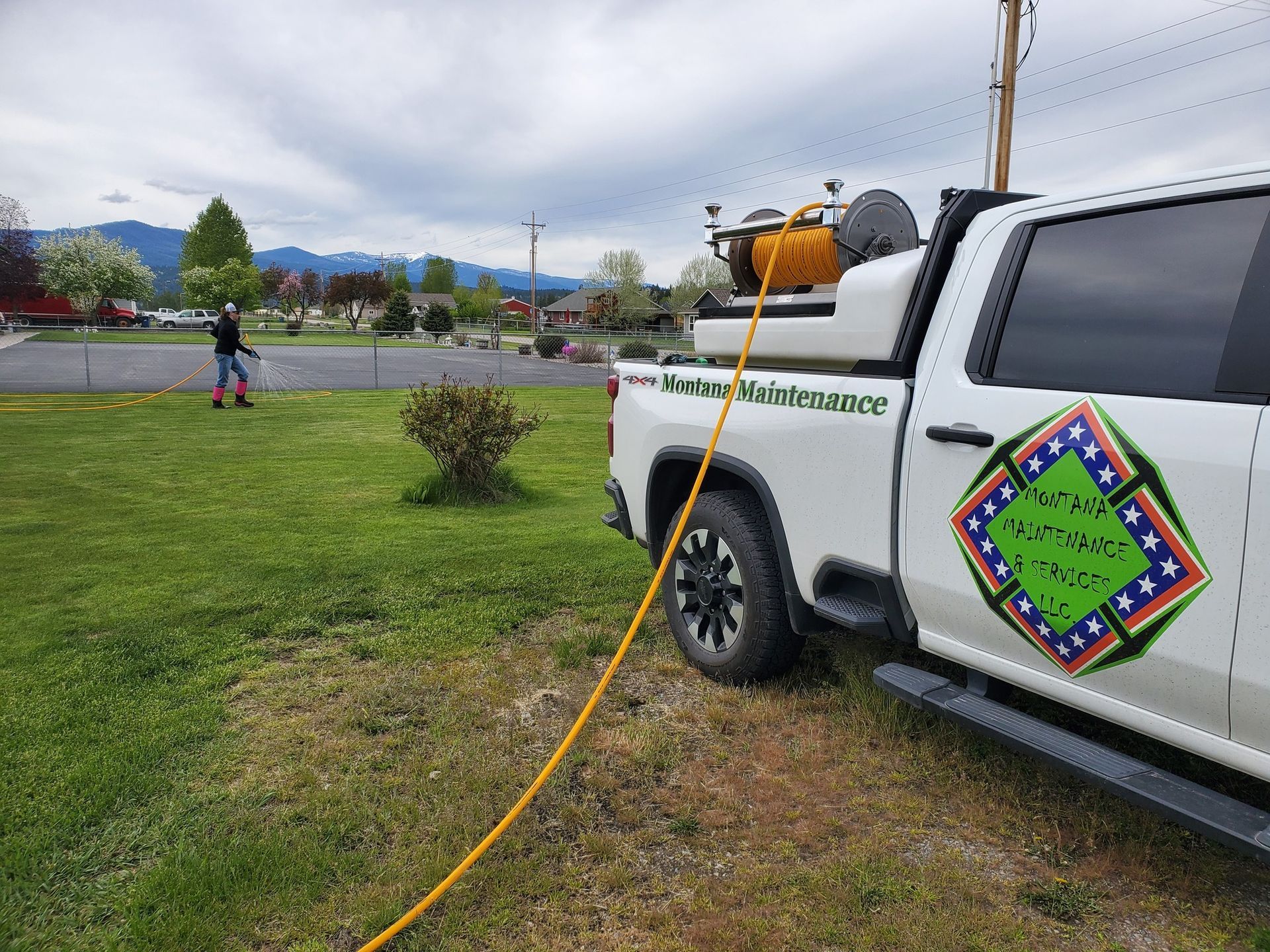 A white truck with a hose spraying a lawn; a person is spraying the grass.