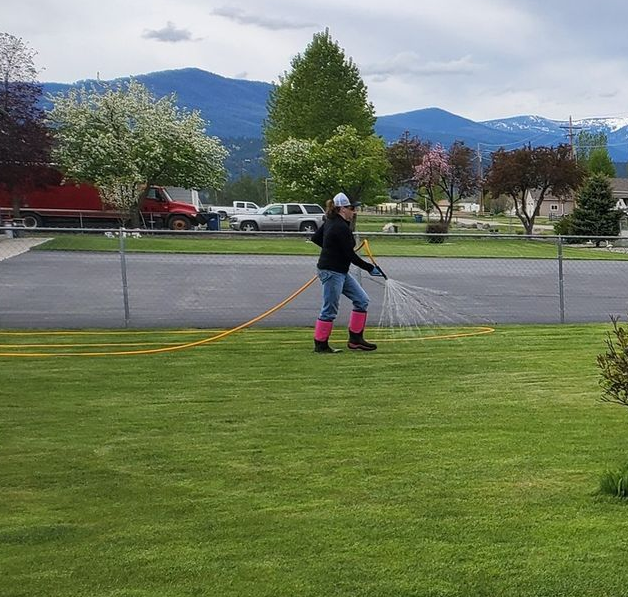 A white truck with a hose spraying a lawn; a person is spraying the grass.