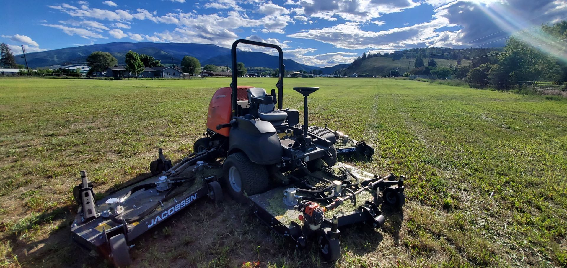 A riding lawn mower in a field with mountains in the background on a sunny day.