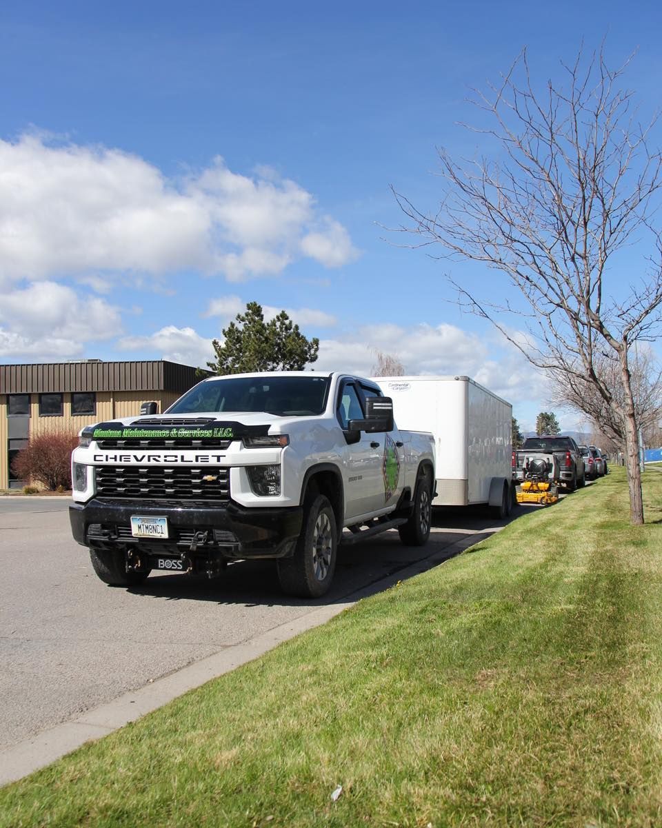 White Chevy truck towing a trailer parked on the side of a road with other vehicles; sunny day.