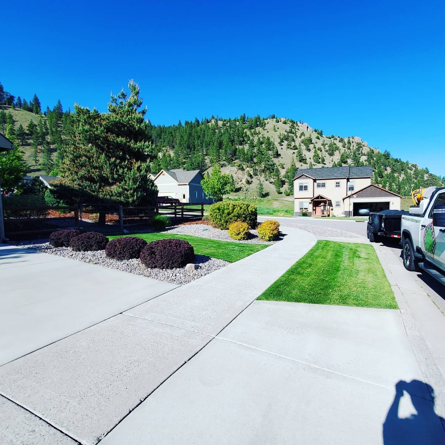A sunny day scene: A well-manicured lawn and walkway leading to a house with a mountain backdrop.