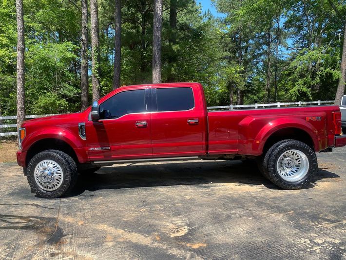 A red truck is parked in a parking lot next to trees.