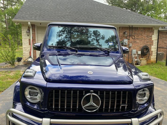 A blue mercedes benz g63 is parked in front of a brick house.