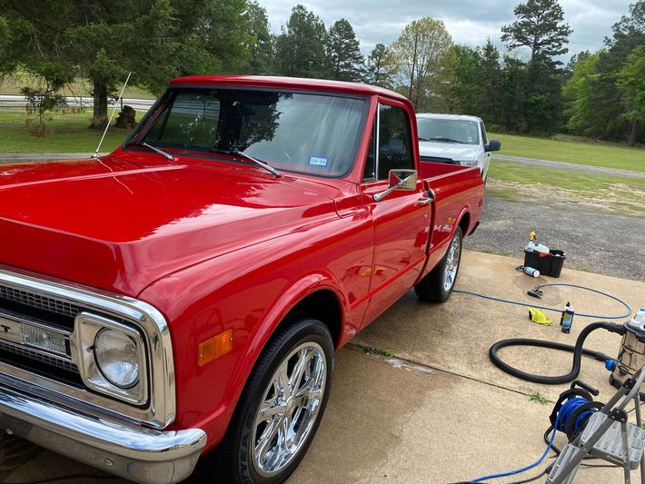 A red truck is parked in a driveway next to a white truck.